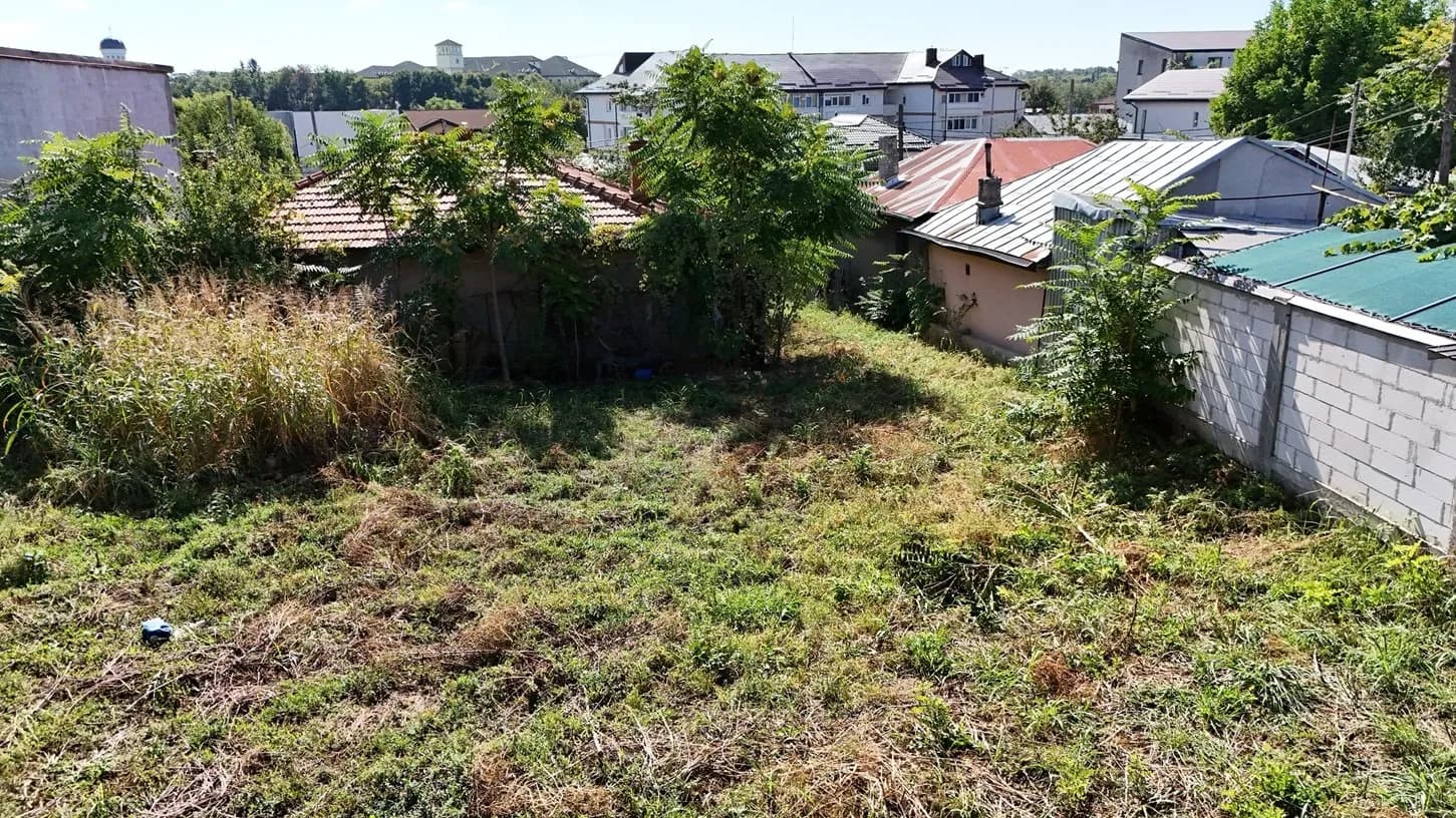 Teren cu iarba crescută, construcții în jur