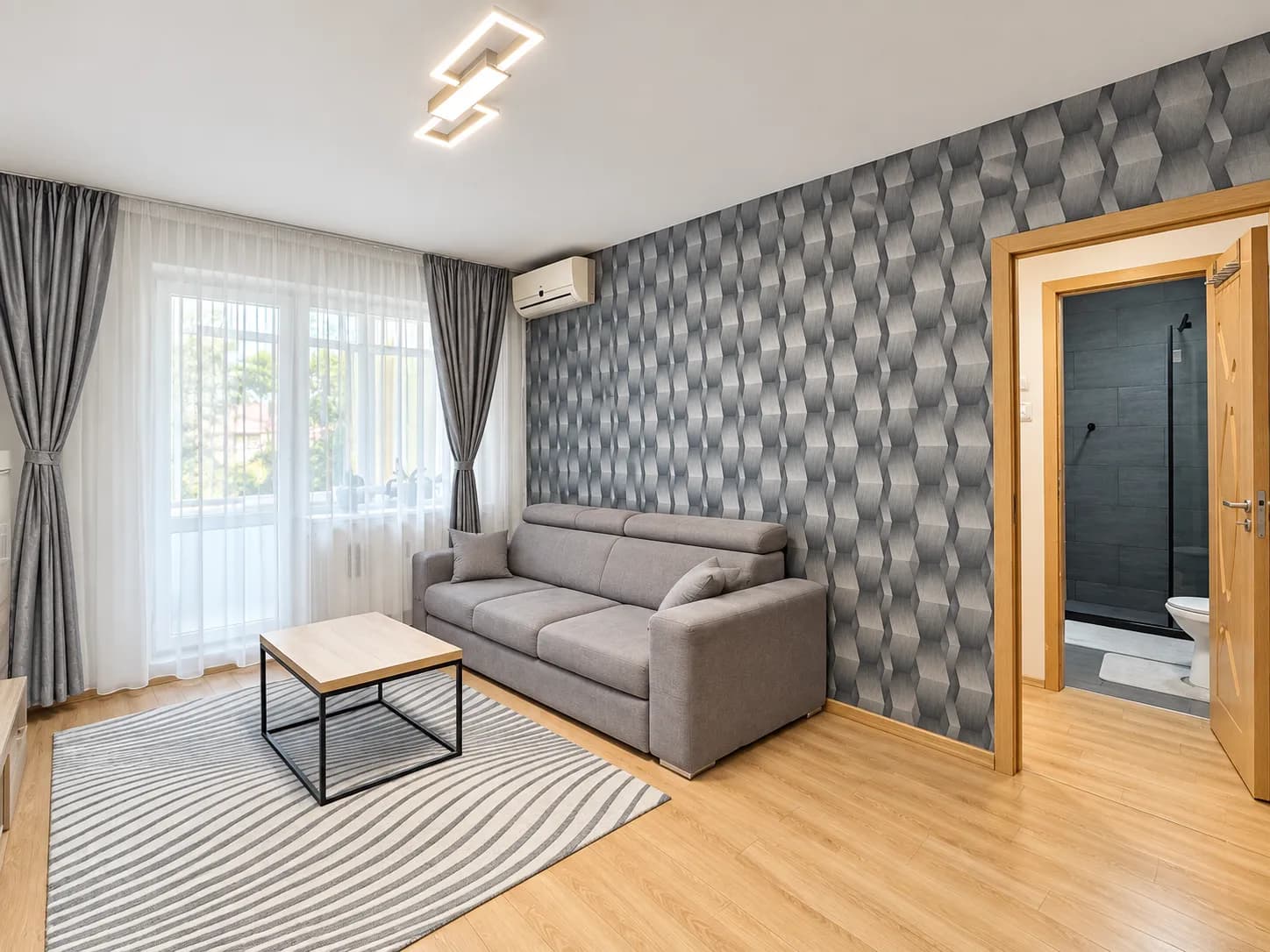 Living cu canapea gri, tapet geometric, acces balcon
