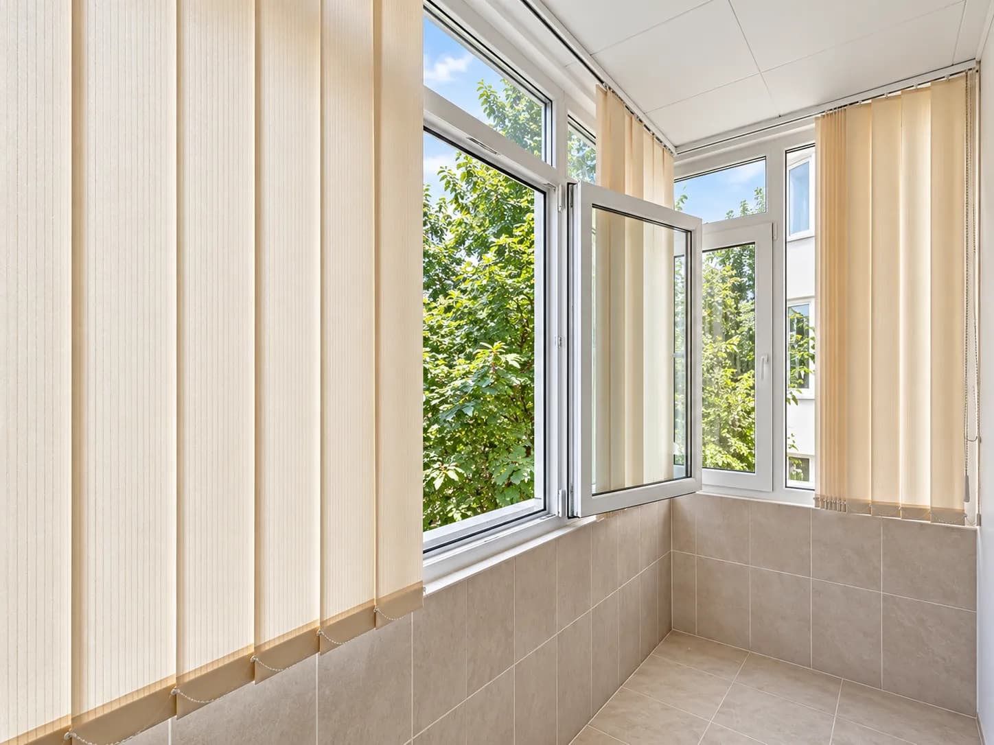 Balcon cu gresie, geamuri larg deschise, perdele bej