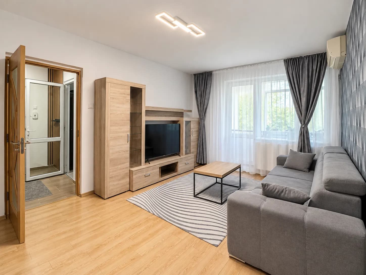 Living cu canapea gri, mobilier lemn și TV