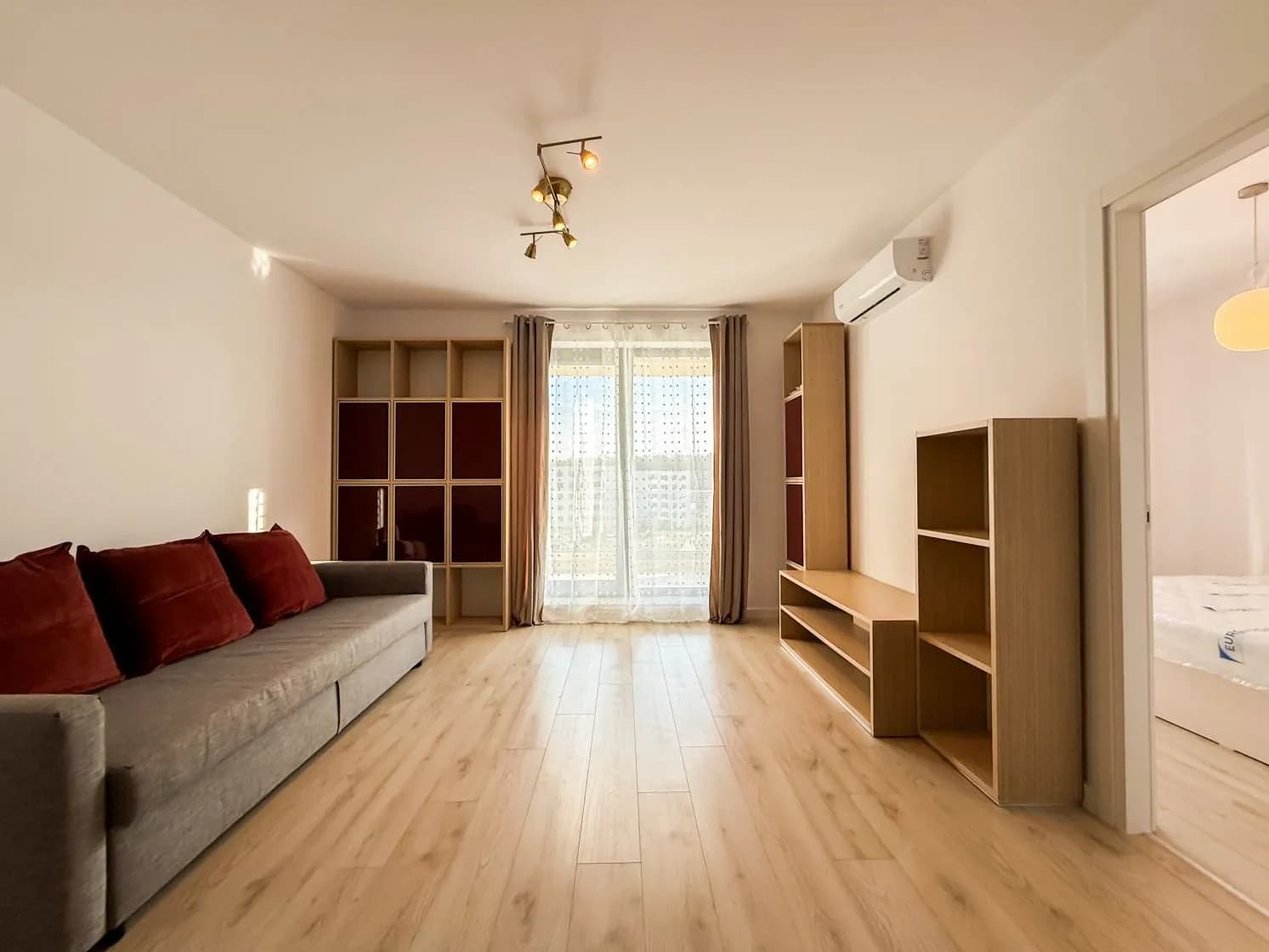 Living cu mobilă gri, perne roșii, parchet și balcon